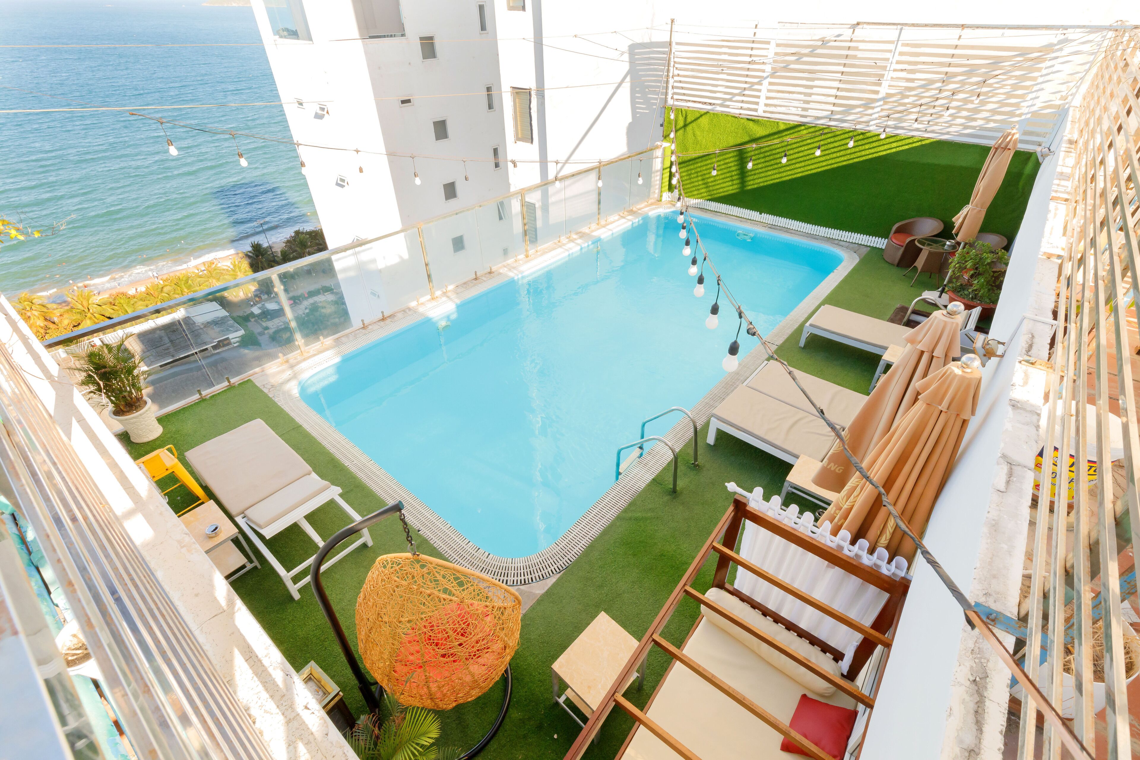 A rooftop pool with a clear view of the ocean, surrounded by lounge chairs and a hanging chair.