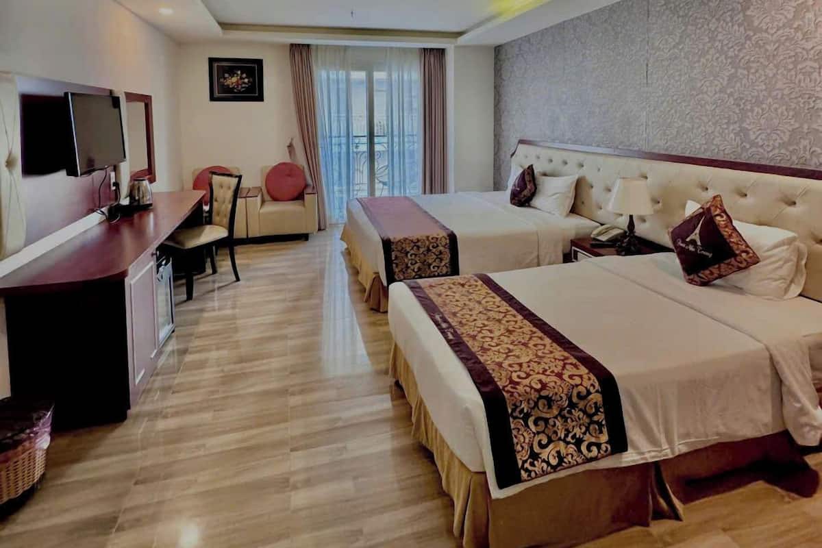 A hotel room with two beds, a desk with a TV, a chair, and a view of the city through large windows.