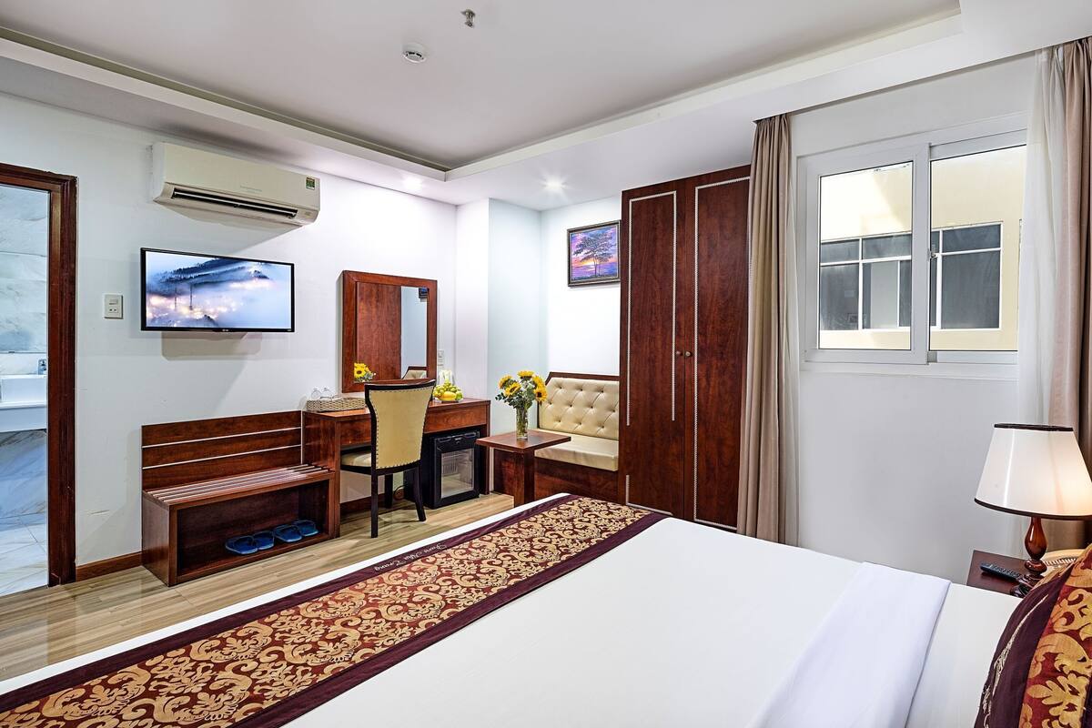 A hotel room with a bed, a desk with a chair, a television, a window with curtains, a lamp, and a bathroom with a mirror and sink.