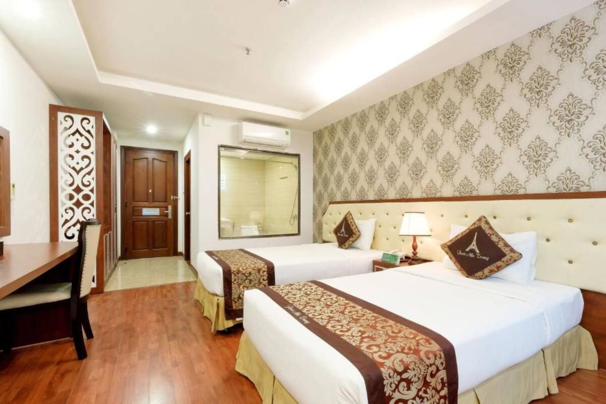 A hotel room with two beds, a desk, and a chair. There is a mirror, a window, and a wall with a patterned design.