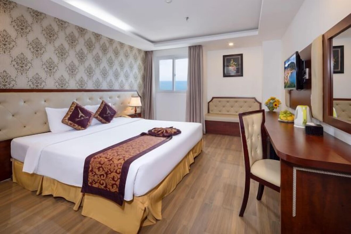 Una habitación de hotel con una cama grande, un escritorio y vistas al mar.
