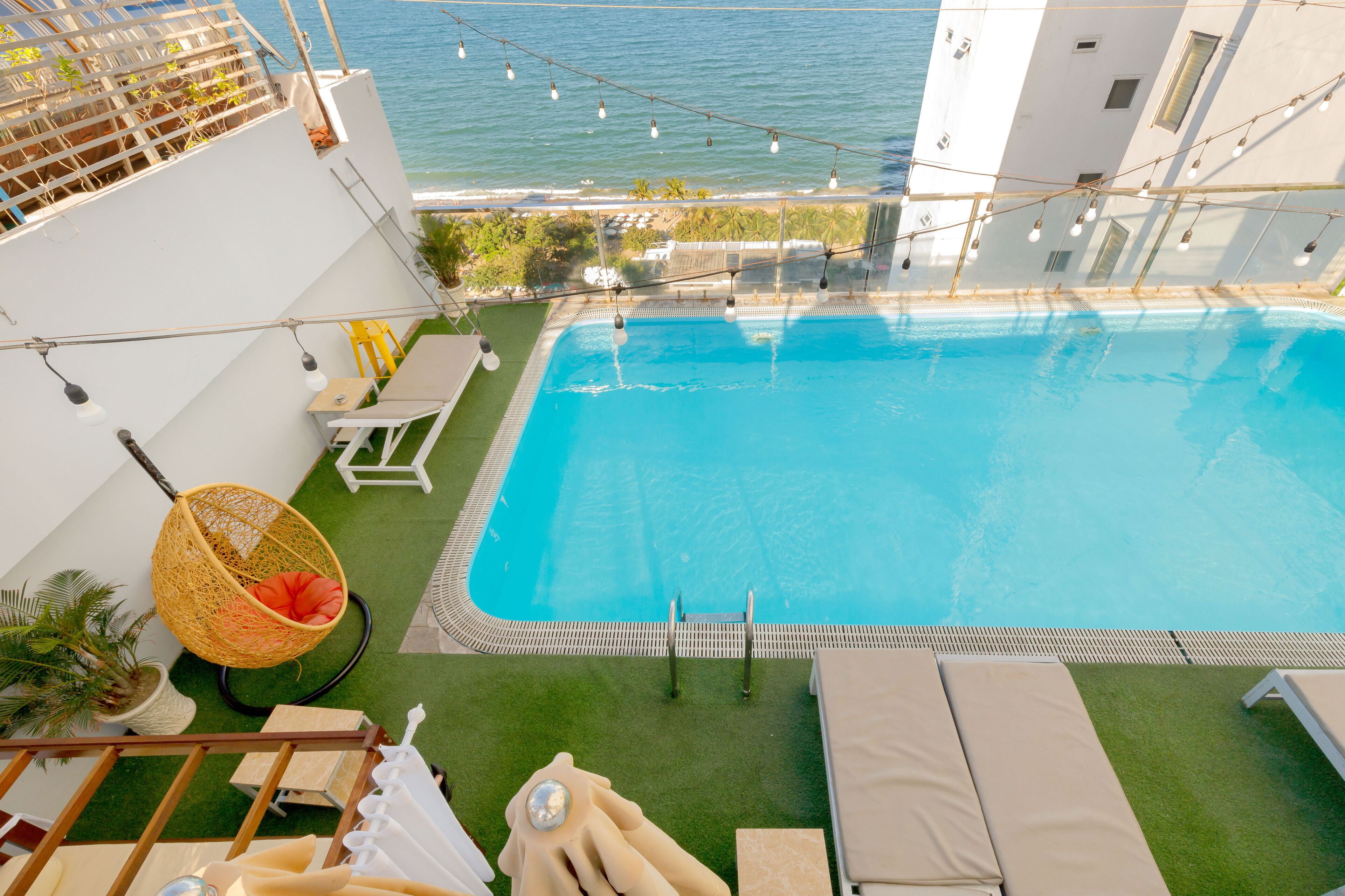 A rooftop pool with a view of the sea, surrounded by lounge chairs and a hanging chair.