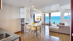 A modern hotel room with a dining area, a sofa, and a view of the sea.
