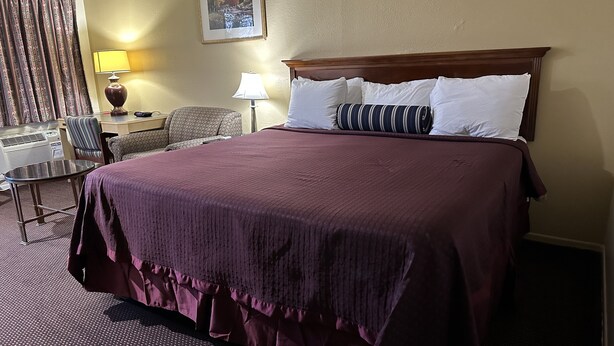 A hotel room with a large bed, a desk with a lamp, a chair, and a window with curtains.