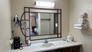 A bathroom with a large mirror, a sink, a coffee maker, and towels on a rack.