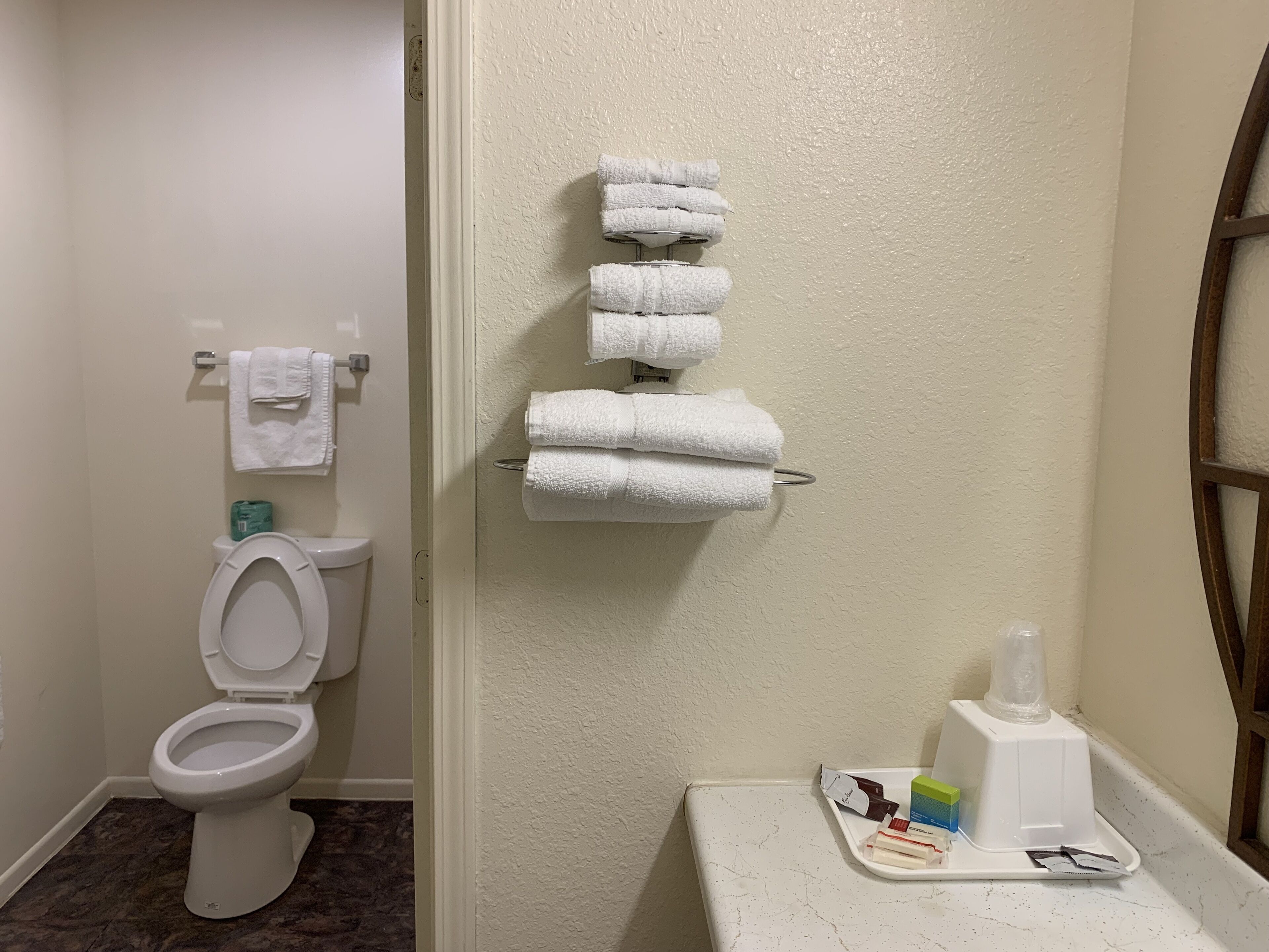 A bathroom with a toilet, a towel rack with folded towels, and a tray with toiletries.