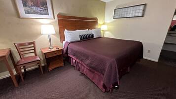 Ett hotellrum med en säng, ett nattduksbord, en stol, ett skrivbord och en lampa.