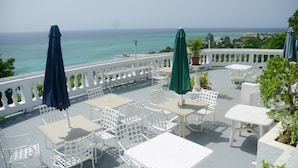 An outdoor patio with white tables and chairs, green umbrellas, and a view of the ocean. - Skymiles Beach Suite At  Montego Bay Club Resort (Montego Bay)