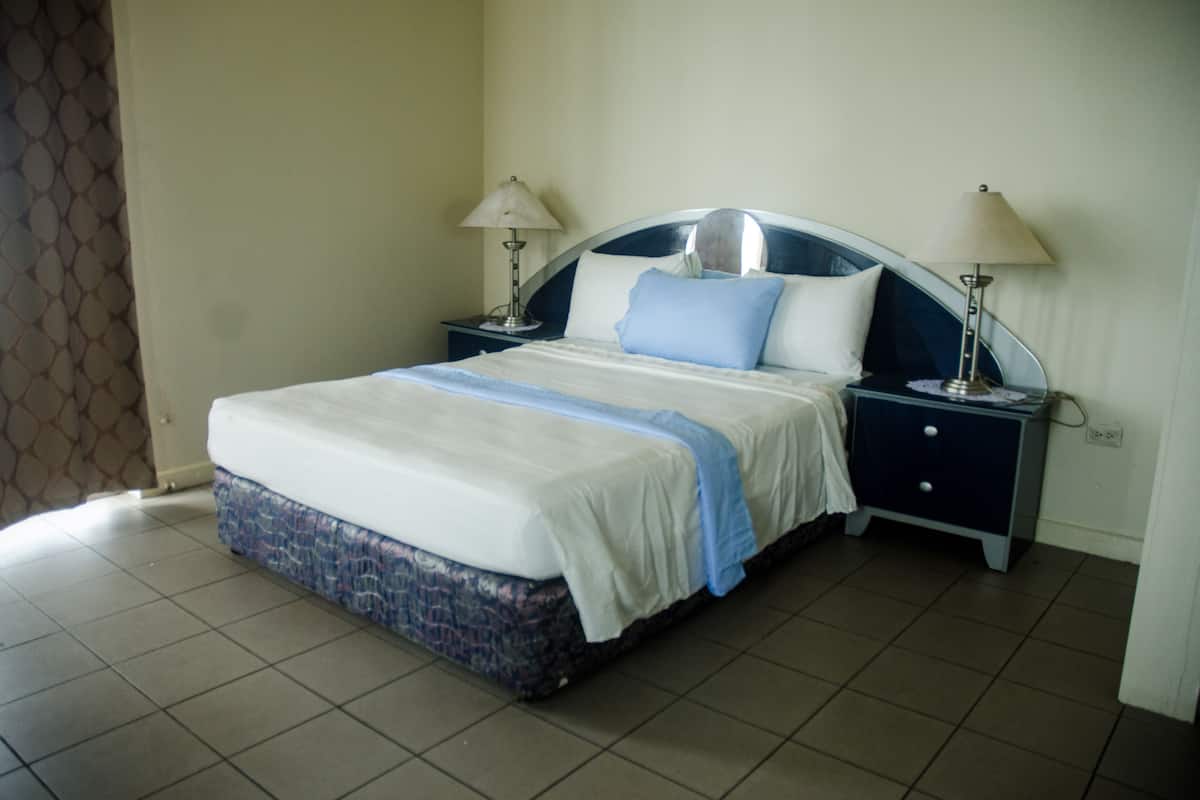 A neatly made bed with a blue and white bedspread, two bedside tables with lamps, and a tiled floor.