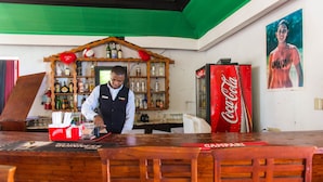 A bar area with a bartender, shelves of liquor, a Coca-Cola refrigerator, and a poster of a Jamaican athlete. - Skymiles Beach Suite At  Montego Bay Club Resort (Montego Bay)