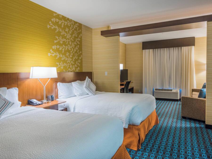 A hotel room with two beds, a desk, a chair, and an air conditioning unit.