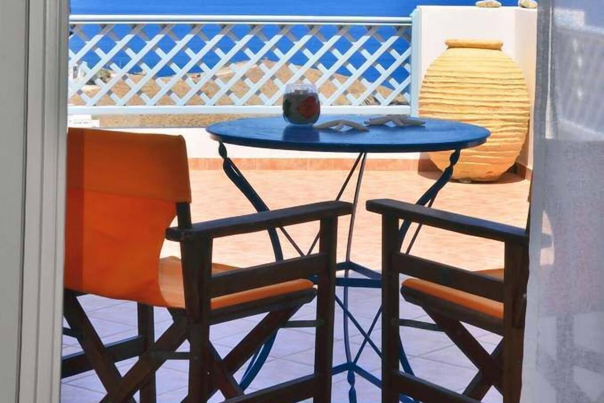 A balcony with a table and chairs, overlooking a clear blue sea and distant land.