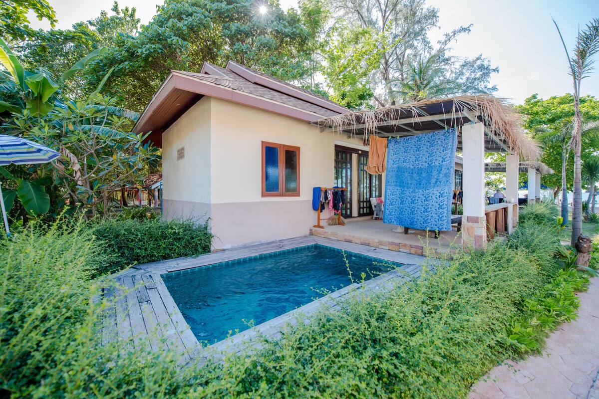 A poolside area with a small pool, a covered seating area, and lush greenery.