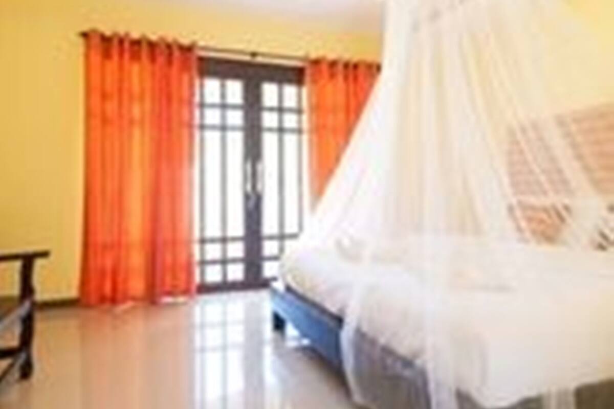 A bedroom with a bed covered by a white canopy, orange curtains, and a large window.