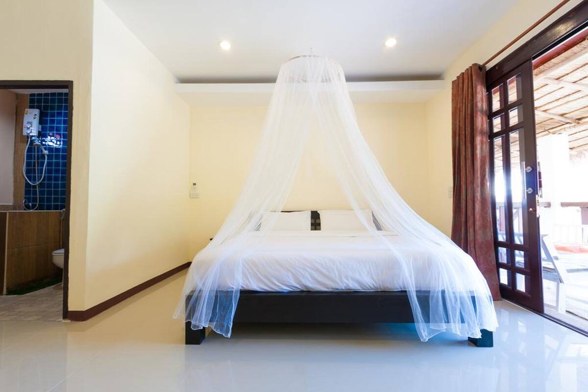 A bedroom with a bed under a white canopy, a wooden door, and a view of the outside.