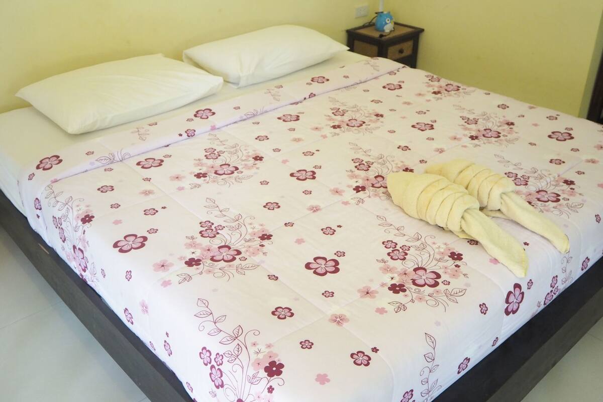 A bed with a floral bedspread, two pillows, and a towel arranged on it.