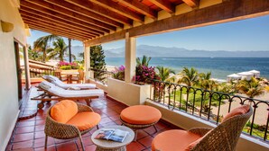 A balcony with wicker furniture, a table with a magazine, and a view of the sea and mountains. - Family Luxury Suites by Velas Vallarta - All Inclusive (Puerto Vallarta)