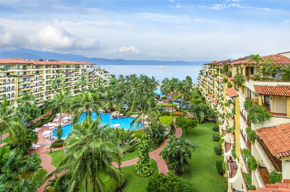 Un resort con varios balcones, una piscina central y abundante vegetación.