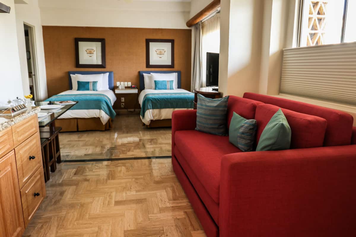 Habitación de hotel con dos camas, un sofá rojo, suelo de madera y un televisor.