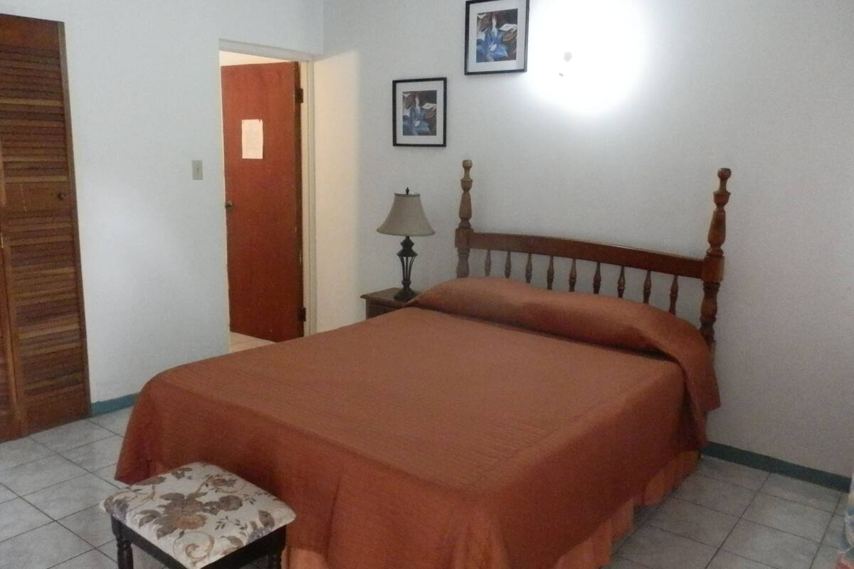 A bedroom with a bed, a nightstand, a lamp, a chair, and a door.