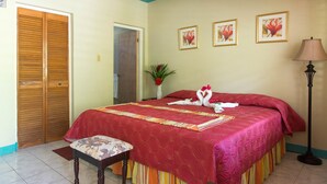 Una habitación de hotel con una cama grande, una puerta de madera, una mesita de noche, una lámpara y tres cuadros en la pared.