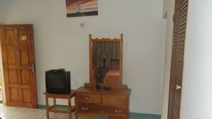 Una habitación con un tocador de madera, un televisor sobre una mesita y una cama.