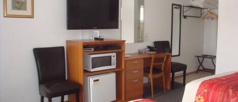 Quarto de hotel com cama, escrivaninha, computador, televisão, micro-ondas e frigorífico.