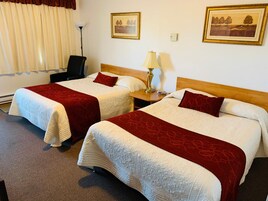 Habitación de hotel con dos camas, cada una con una colcha roja y blanca, un cabecero de madera, una mesita de noche con una lámpara y dos cuadros enmarcados en la pared.