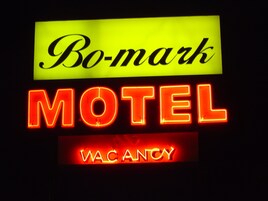 Un letrero de neón con la inscripción "Bo-mark MOTEL" y "VACANCY", indicando un motel con habitaciones disponibles.