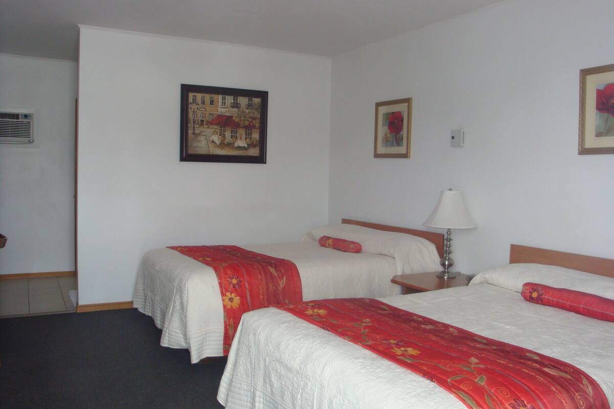 A hotel room with two beds, a nightstand, a lamp, and a wall-mounted air conditioning unit.