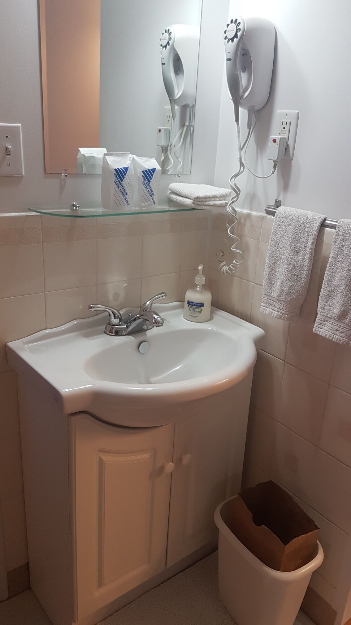 Une salle de bain avec un lavabo blanc, un miroir, un sèche-cheveux et une poubelle.