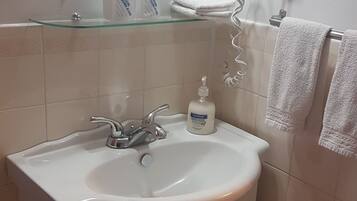 Une salle de bain avec un lavabo blanc, un miroir, un sèche-cheveux et une poubelle.