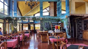 A restaurant with wooden tables and chairs, a brick wall, and a mural on the wall. - Hotel Villa Verde (Monteverde)