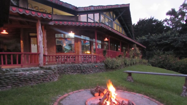 A building with a fire pit in the front yard, a stone wall, and a red railing. - Hotel Villa Verde (Monteverde)
