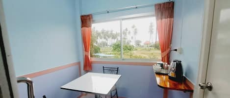 Una habitación pequeña con una mesa, sillas, un ventanal con cortinas y vistas al verdor exterior.