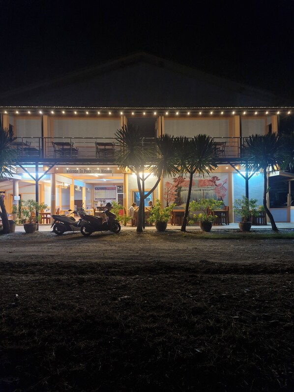 A two-story building with a sign reading "Welcome To Peace Lana Mansion." There are potted plants and a motorcycle parked in front.