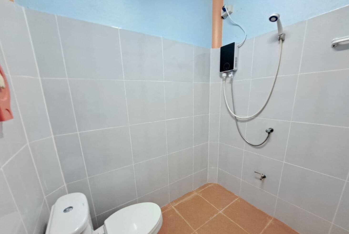 A small bathroom with a toilet, a shower, and a control panel on the wall.
