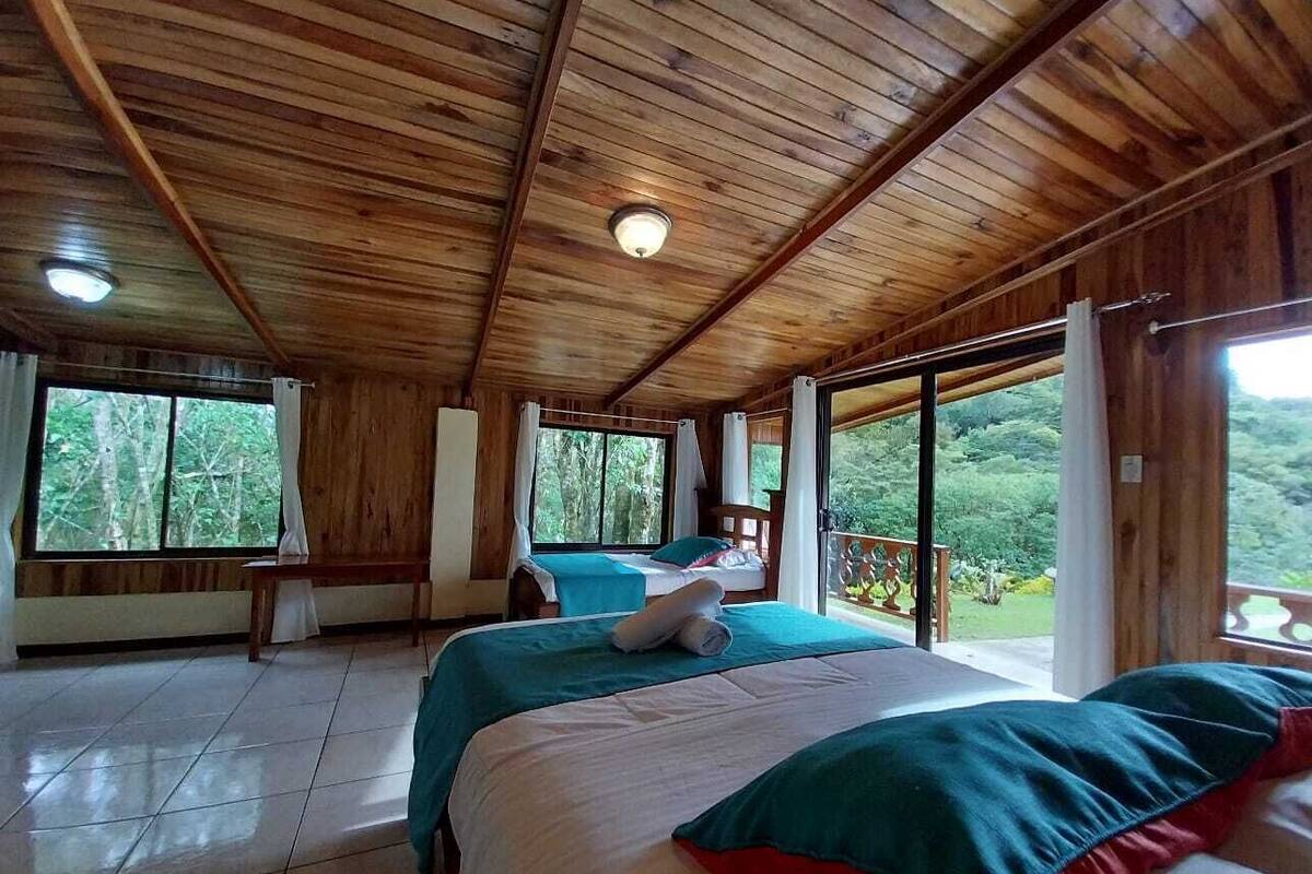 Una cabaña de madera con dos camas, un balcón y ventanas amplias.
