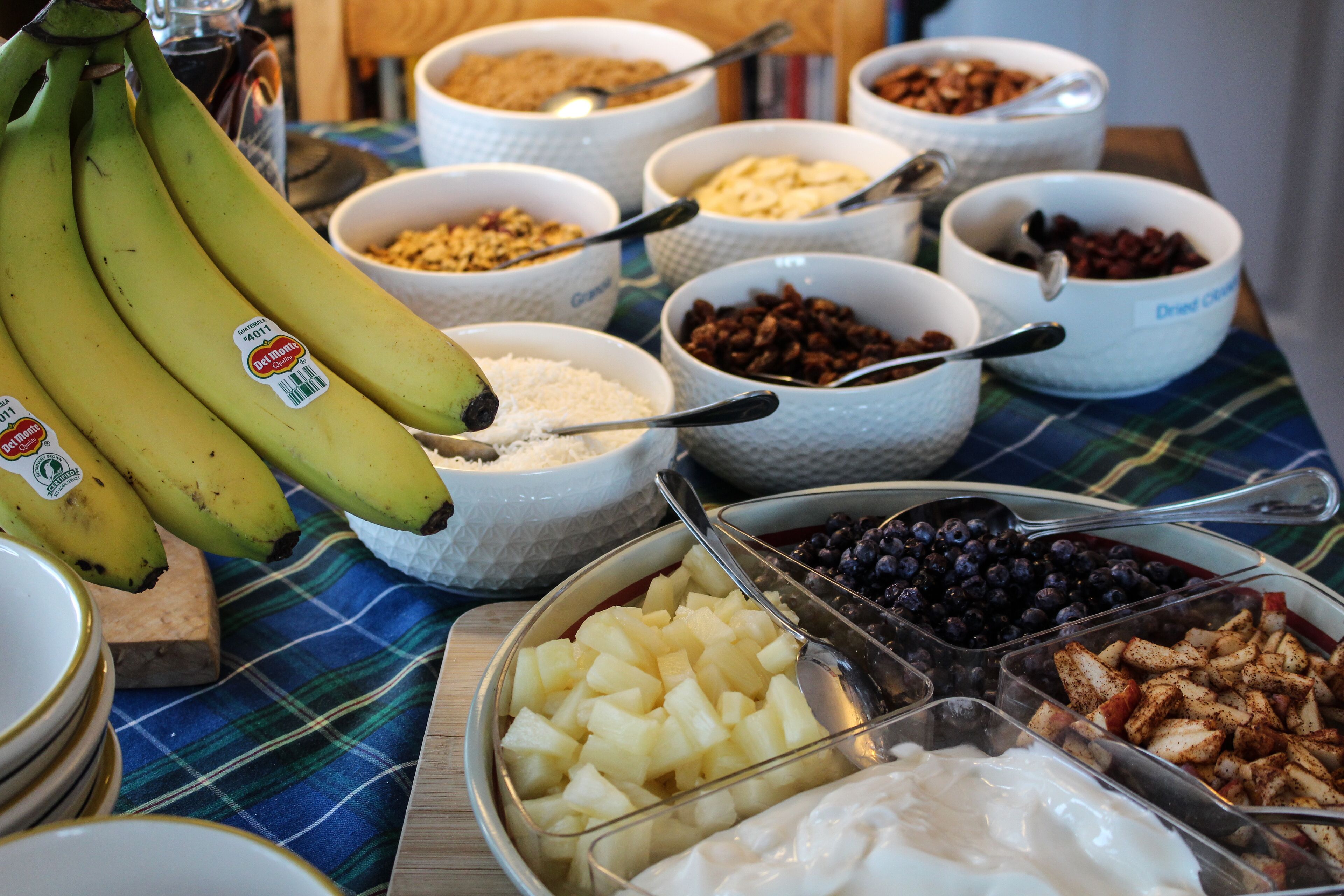 Bufet amb diferents aliments, com ara plàtans, granola, fruits secs i iogurt.