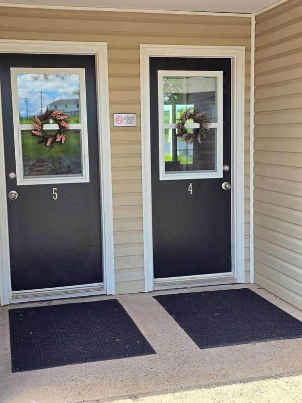 Two black doors with white frames, each with a glass panel and a wreath. A 'No Smoking' sign is visible on the wall. - Antigonish Evergreen Inn (Sylvan Valley)