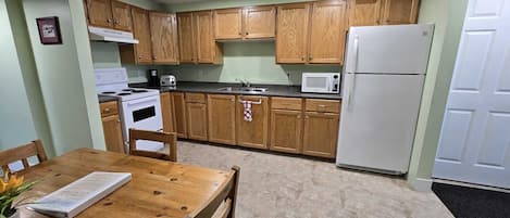A compact kitchen with wooden cabinets, a white stove, a microwave, and a refrigerator.