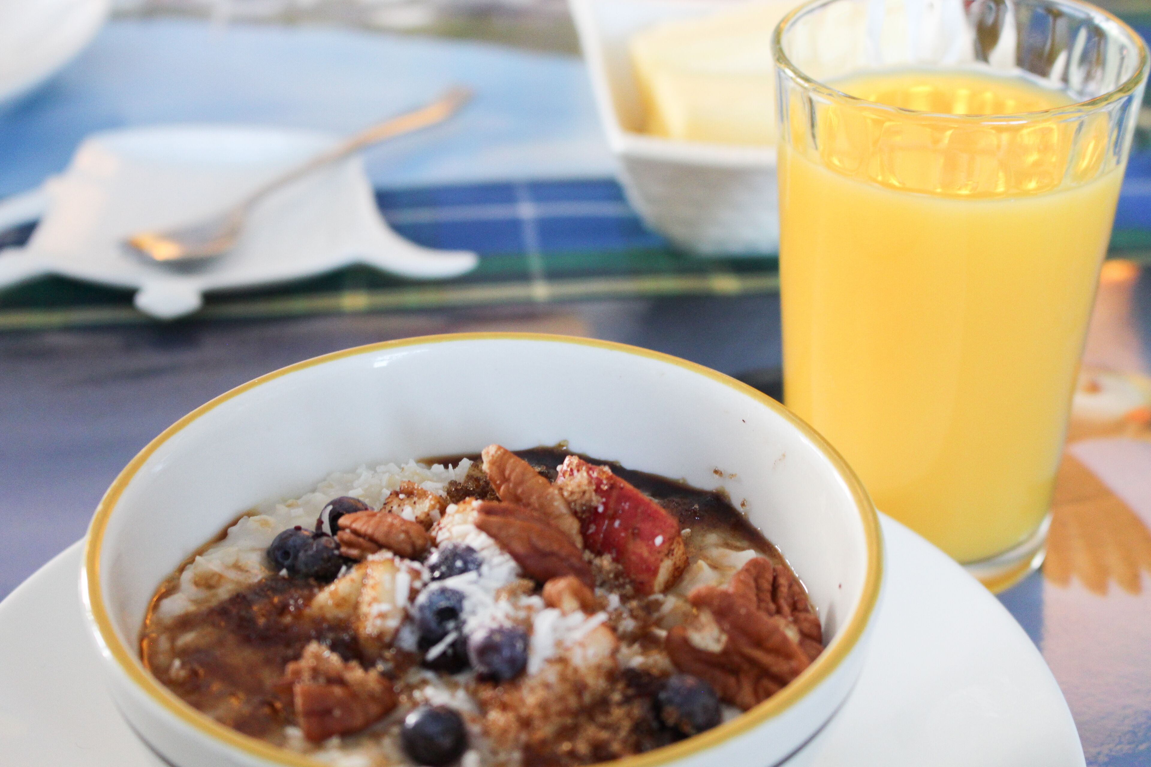 A bowl of oatmeal with blueberries and pecans, a glass of orange juice, and a white plate with a spoon.