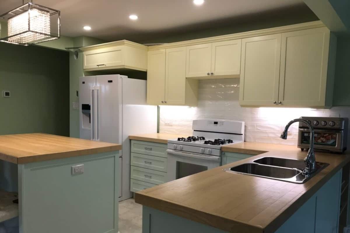 A kitchen with light green cabinets, a white refrigerator, a stove, and a sink.
