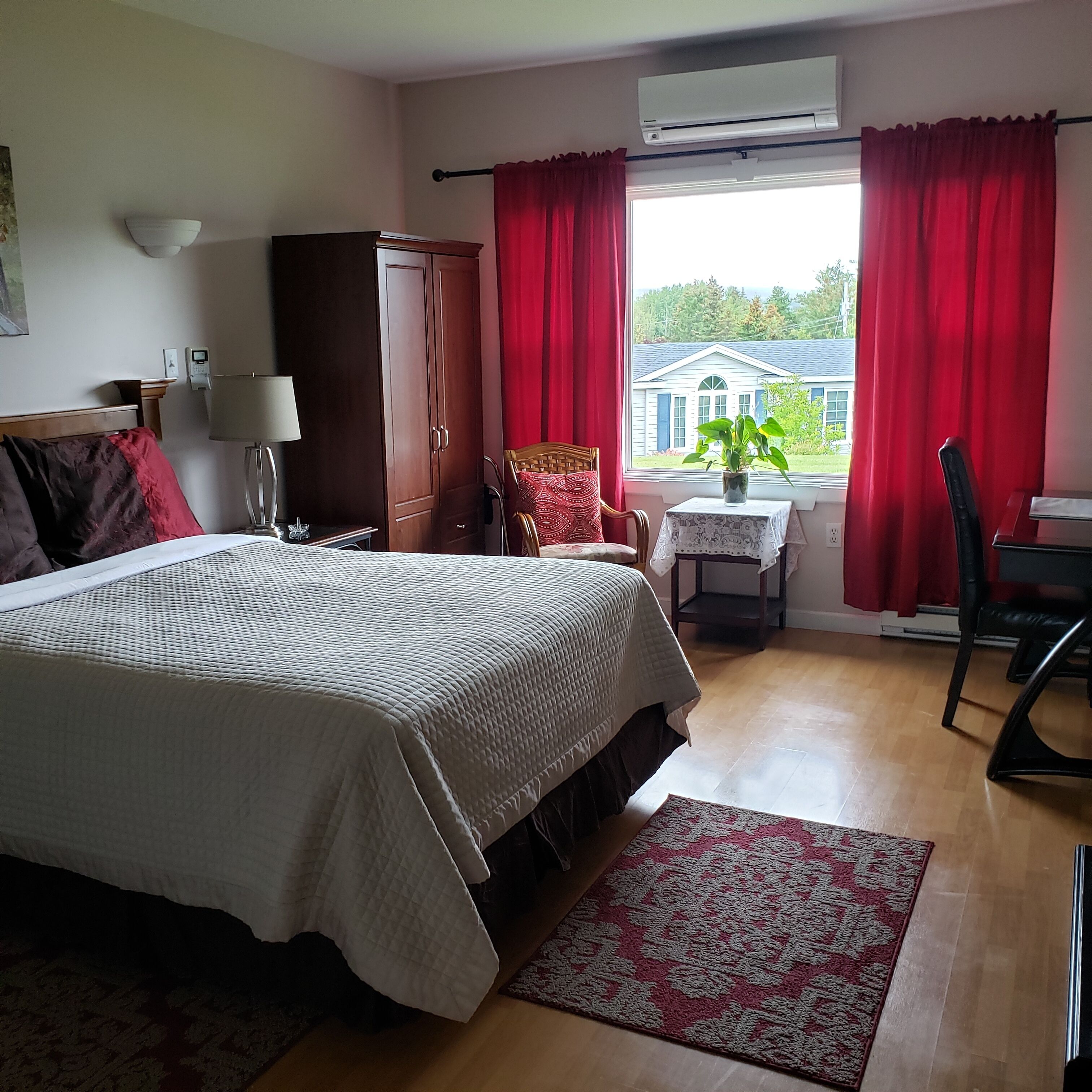Un dormitorio con cama, escritorio, silla, armario y ventana con cortinas rojas.