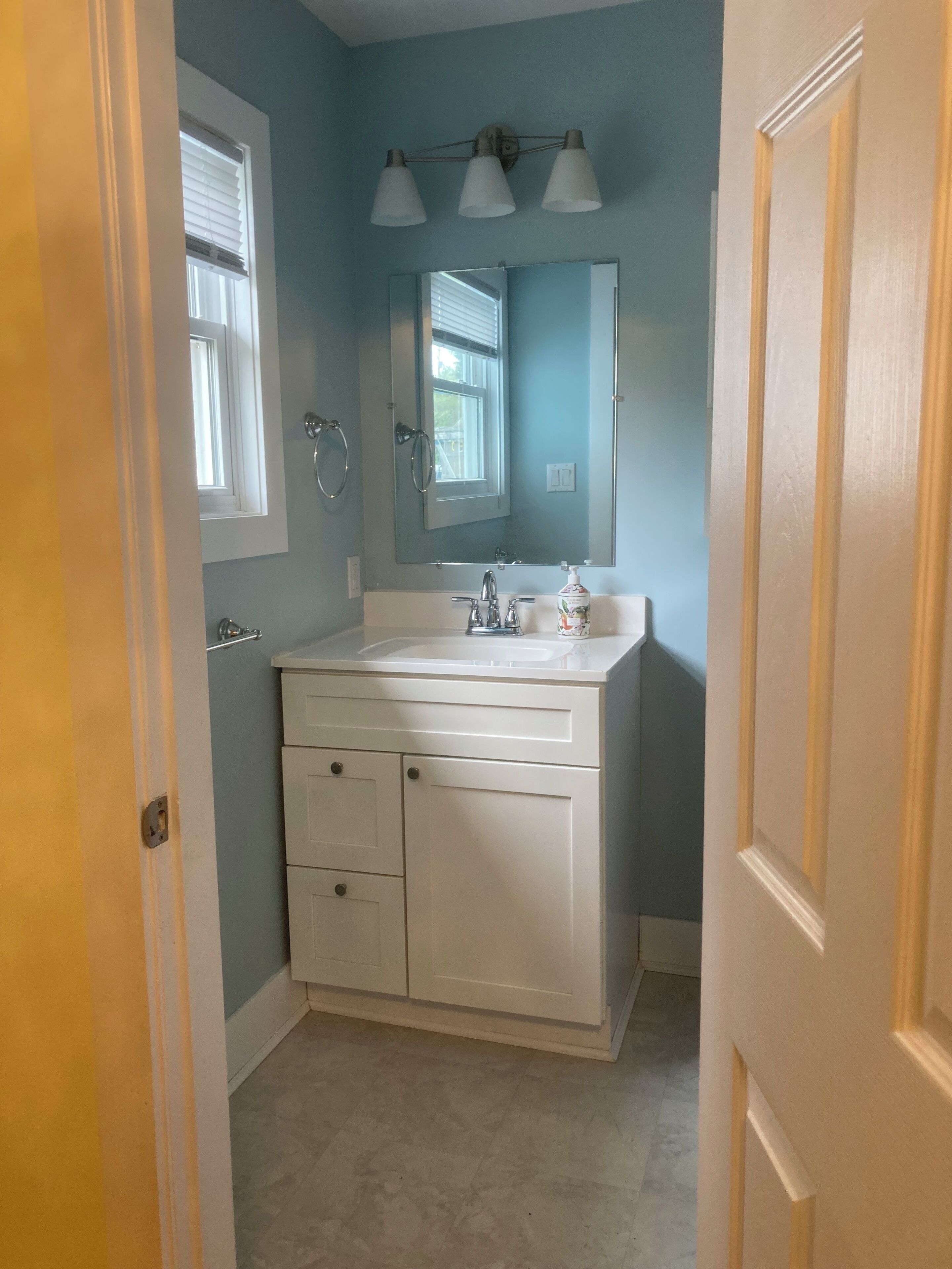 Un baño con tocador blanco, espejo y ventana.