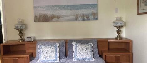 Een slaapkamer met een bed, twee nachtkastjes, een klok en een schilderij aan de muur.