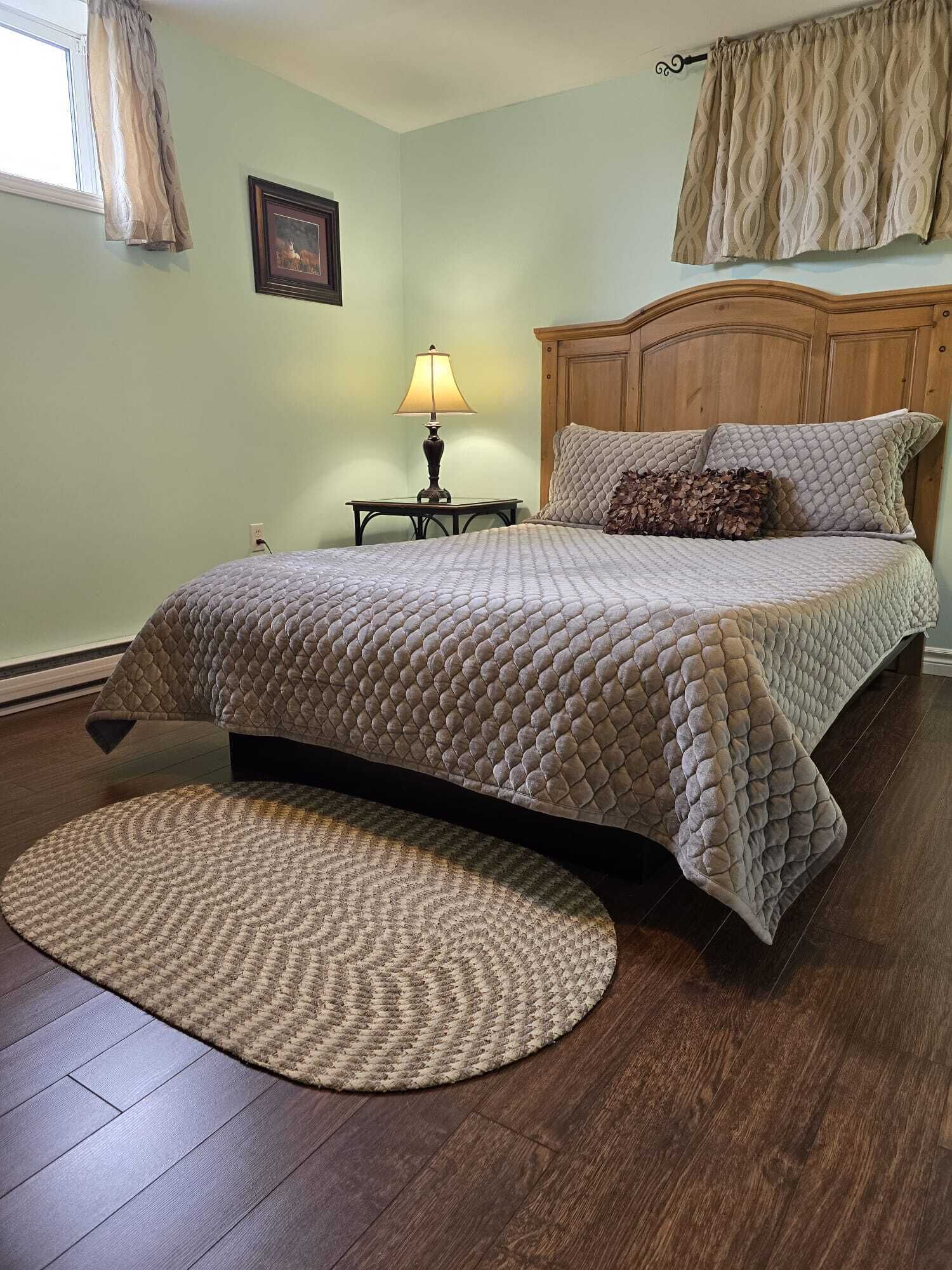 A bedroom with a bed, a nightstand, a lamp, a round rug, and a wooden headboard.
