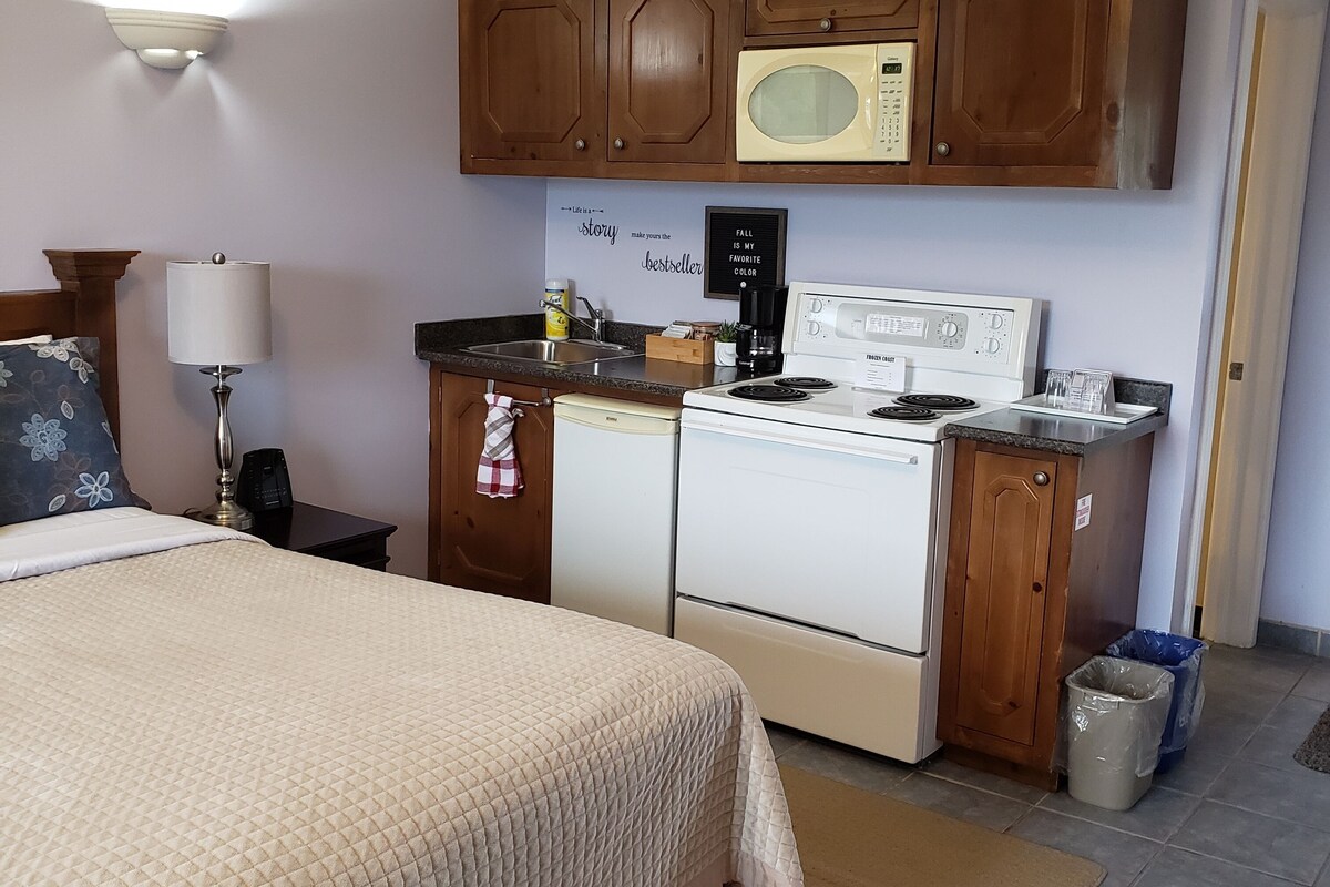 A compact hotel room with a bed, kitchenette, and a small bathroom.
