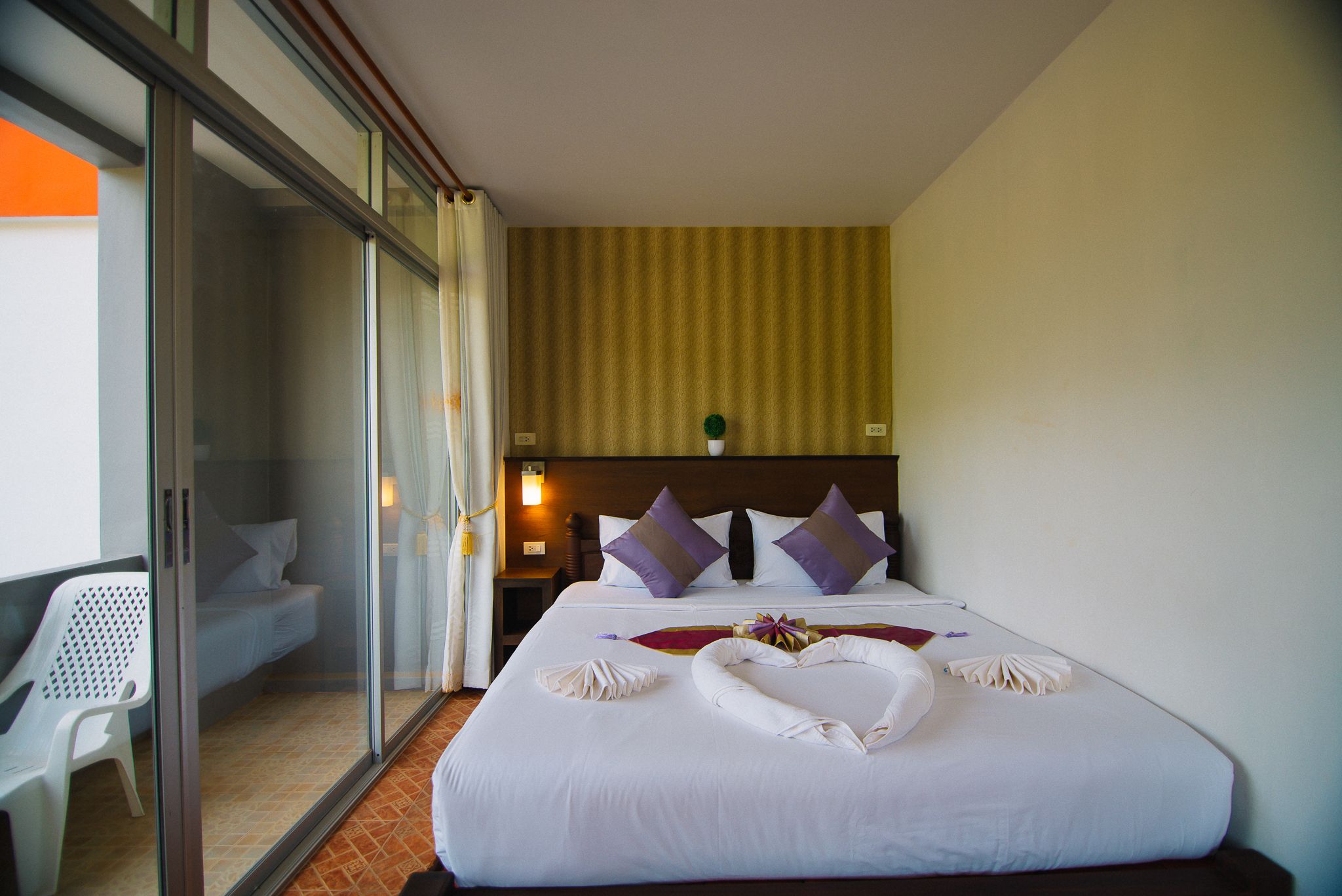 Une chambre d’hôtel avec un lit, une porte vitrée donnant sur un balcon et une table de chevet avec une lampe.