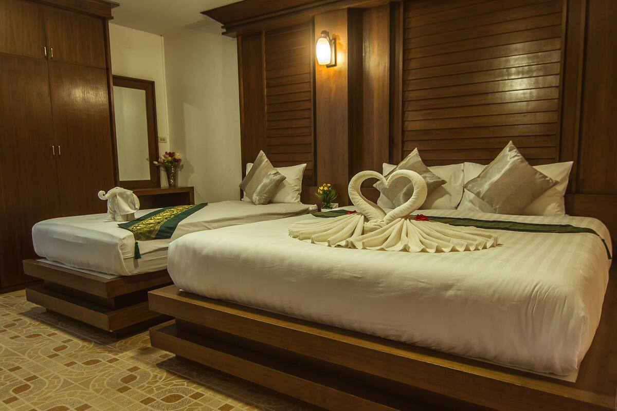 Quarto de hotel com duas camas, painéis de madeira, uma mesinha de cabeceira, um vaso com flores e uma luminária na parede.